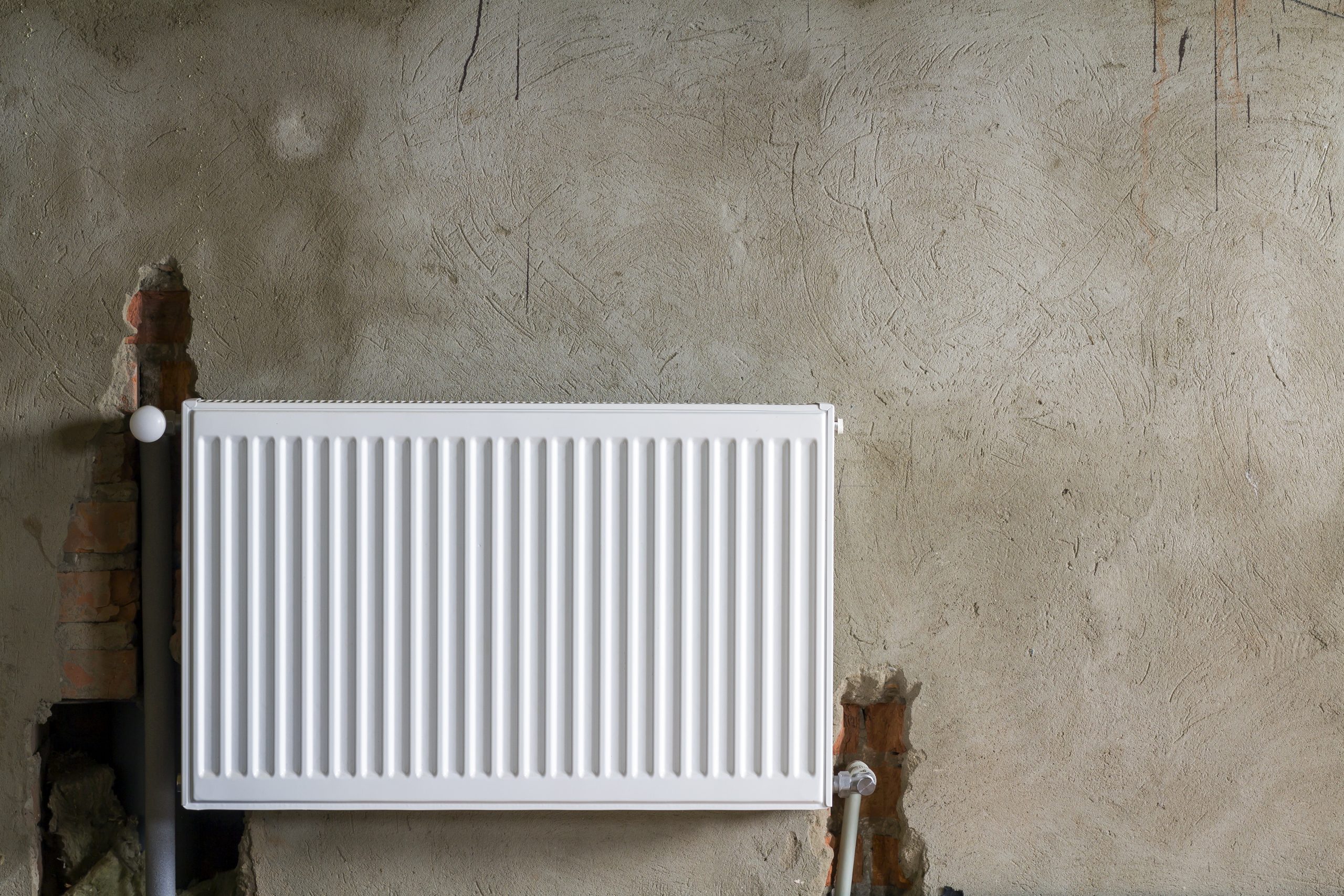 Close-up view of new isolated installed heating radiator on brick rough plastered wall in an empty room of a newly built apartment or house. Construction, maintenance, plumbing and repairing concept.